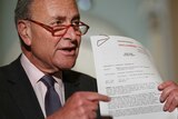 Chuck Schumer holds and points to a document that has UNCLASSIFIED printed on it in red.