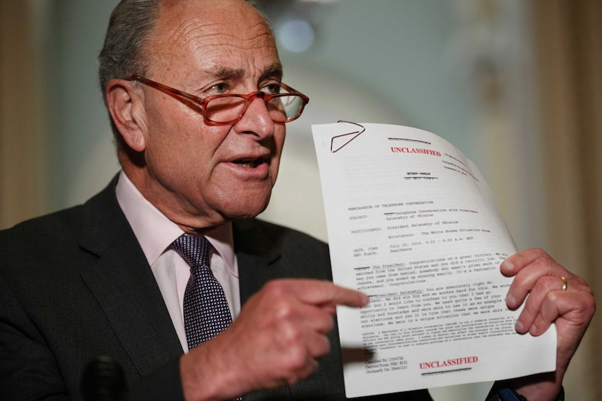 Chuck Schumer holds and points to a document that has UNCLASSIFIED printed on it in red.