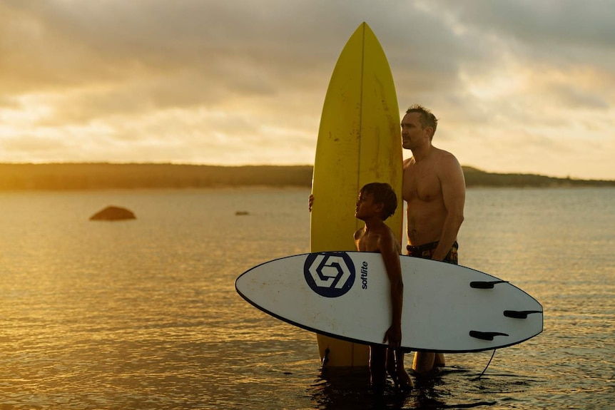 Surfers Tyren Smith and Tim Blake stand, surfboards at the ready, in shin-deep ocean waters surrounding north-east Arnhem Land.