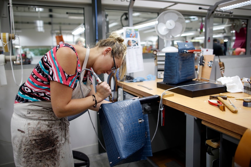 A woman bends over a handbag she is making in a factory