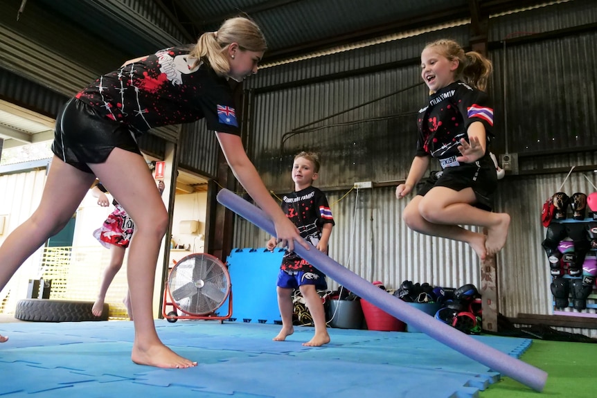 A young girl jumps over a pool noodle during a training session