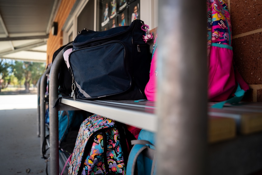 A close-up shot of school bags on a rack outside a classroom.