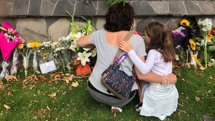 A woman and child kneel in front of a flower covered memorial in the Christchurch Botanic Gardens.