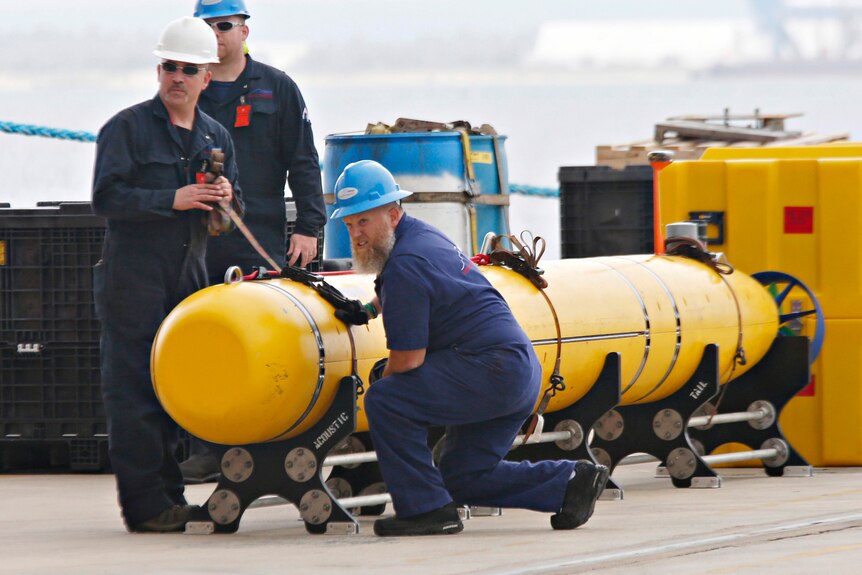 Workers secure a yellow torpedo-looking mapping robot on land. 