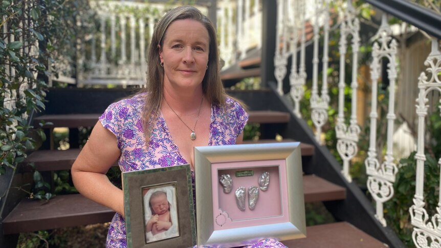 An image of Heidi Mules sitting on stairs with a photo of Sophie and a frame of a mould of the babies feet and hands 