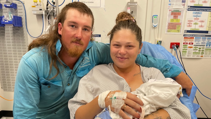 man with mullet and blue shirt hugs woman in hospital gown holding baby