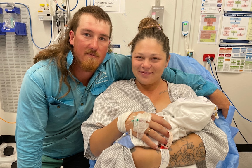 man with mullet and blue shirt hugs woman in hospital gown holding baby