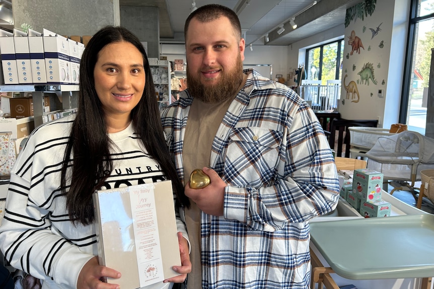 Crystal, holding a pregnancy loss journal, and husband Ryan Zeeman standing in a baby shop in Launceston