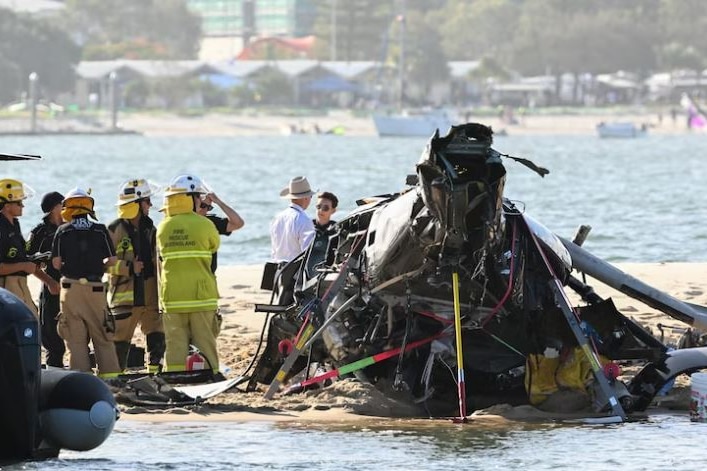 Police and authorities stand inspecting a helicopter crash on a sandbar. 