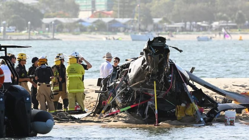 Police and authorities stand inspecting a helicopter crash on a sandbar. 