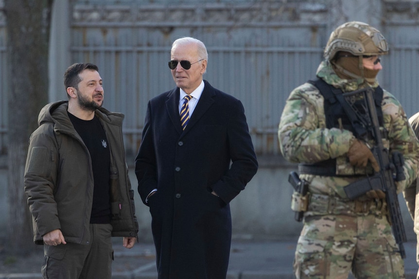 Two men stand togethere as a man in uniform stands by. 