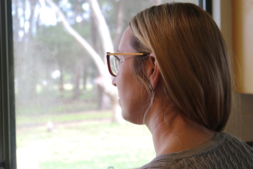 The side view of a women staring out a window into the backyard. 