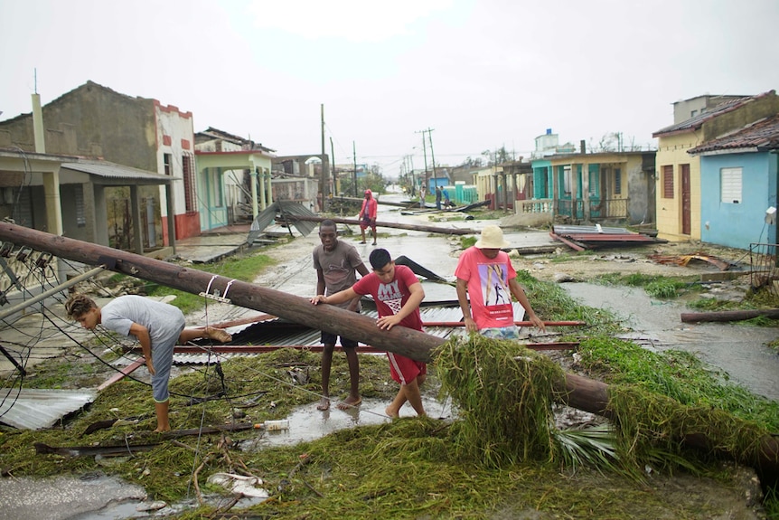 People walk on a damaged street littered with green waste and falled power lines in Cairbarien, Cuba.