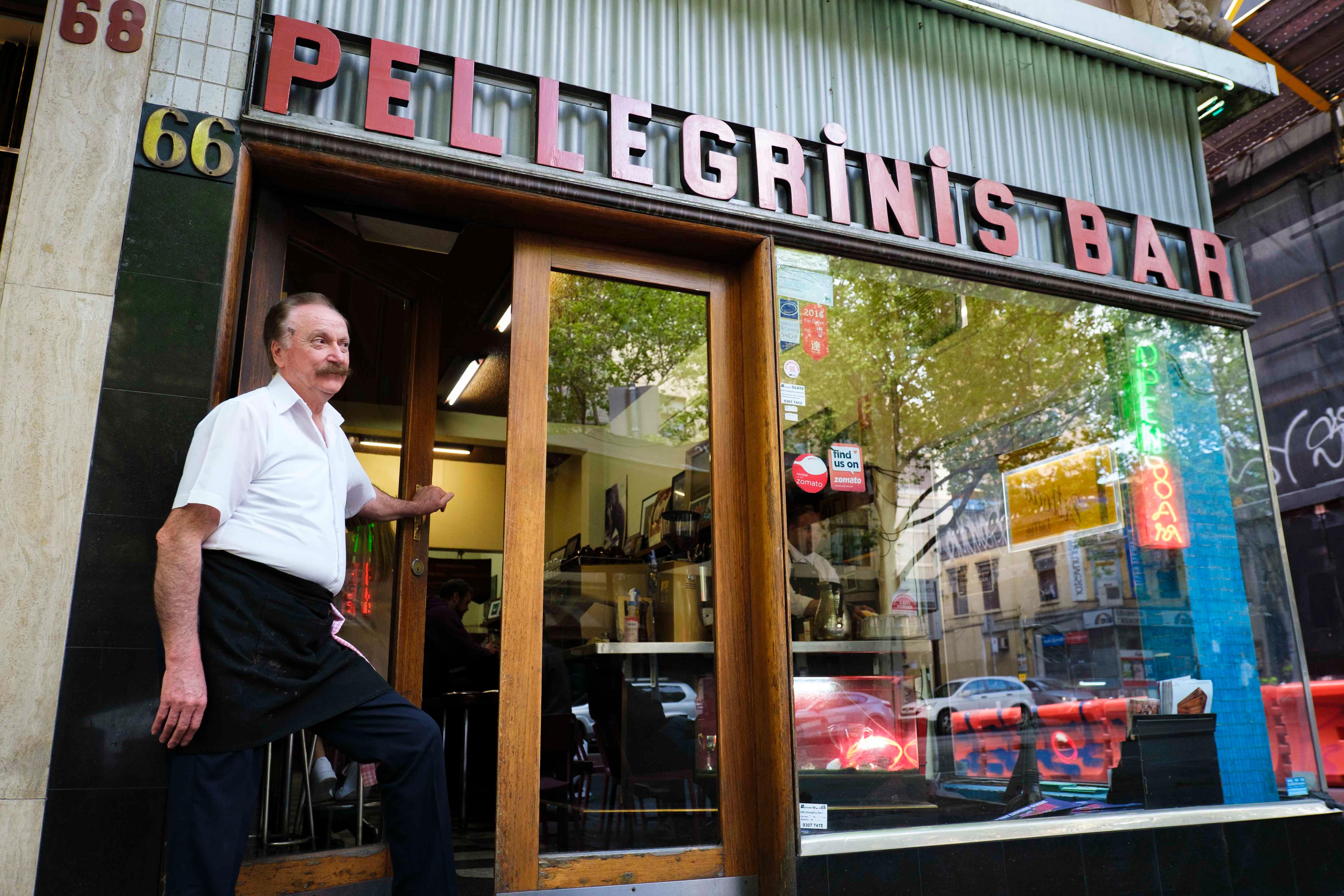 Rocco standing at the entrance of his bar, under a sign reading 'Pellegrini's bar'.