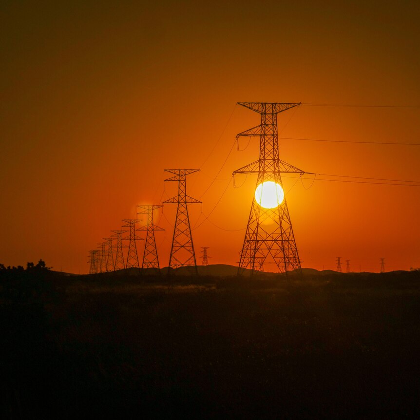 Sun setting through a line of transmission towers