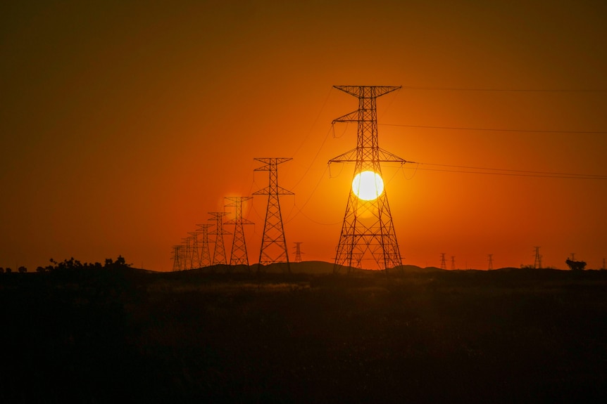Sun setting through a line of transmission towers