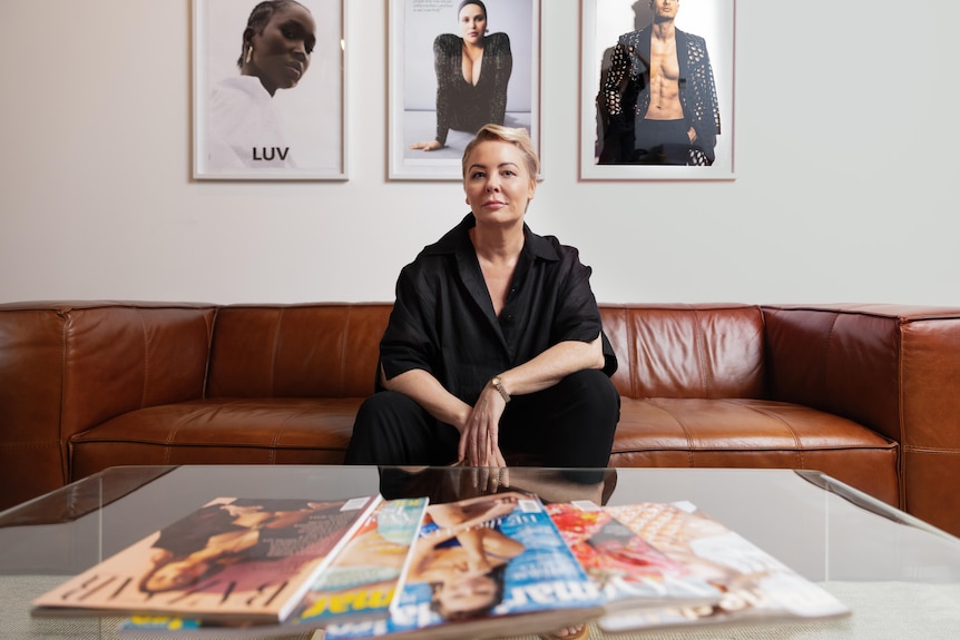 Woman sits on a brown leather couch. In front of her is a coffee table with magazines spread out 