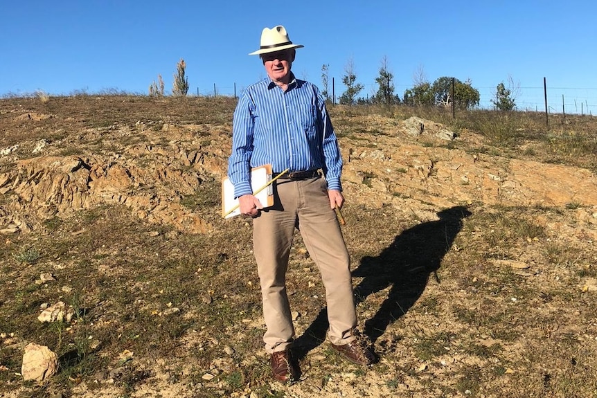 Stuart Burge stands with a clipboard in his hand in a dry paddock