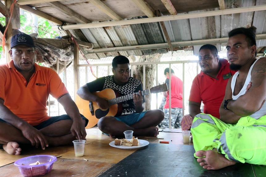 A group of men sing and play guitar