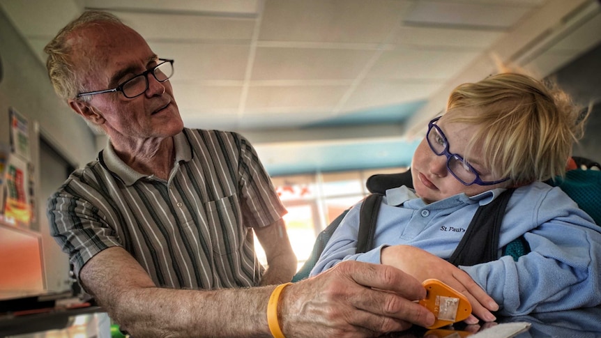 A picture of a young boy in glasses in a wheelchair, with an older man sitting next to him.