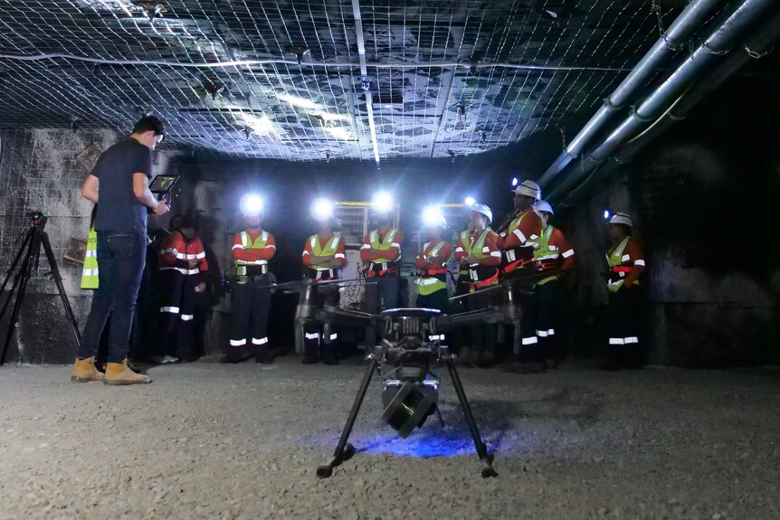 A drone in the foreground in front of a group of mine workers in high-vis gear