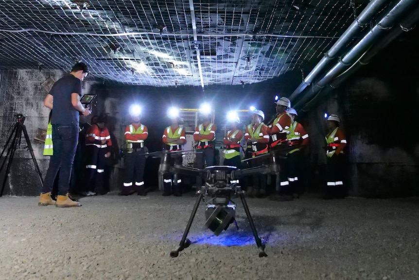 A drone in the foreground in front of a group of mine workers in high-vis gear