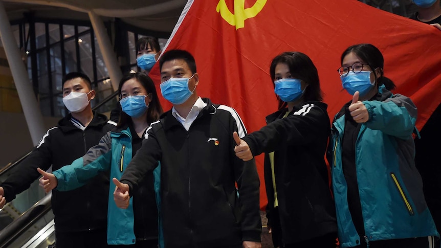 Medical workers from outside Wuhan pose for pictures with a Chinese Communist Party flag