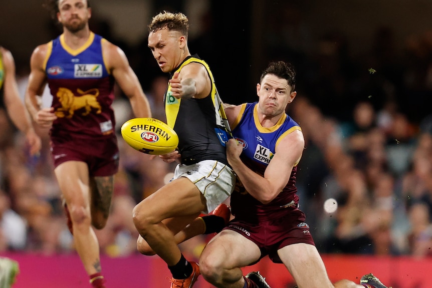 Lachie Neale de Brisbane Lions aborda a Shai Bolton de Richmond, quien deja caer el balón, en un juego final de la AFL.