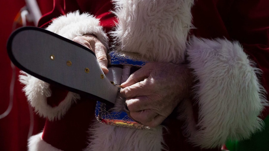 Hands fasten Santa's thick black belt around a red and white suit.