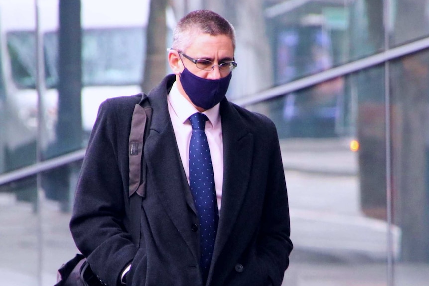 A businessman wearing a suit and tie and a dark mask walks in Melbourne.