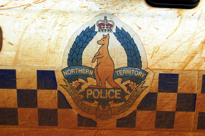 A dust covered Northern Territory Police logo on the side of a police car.