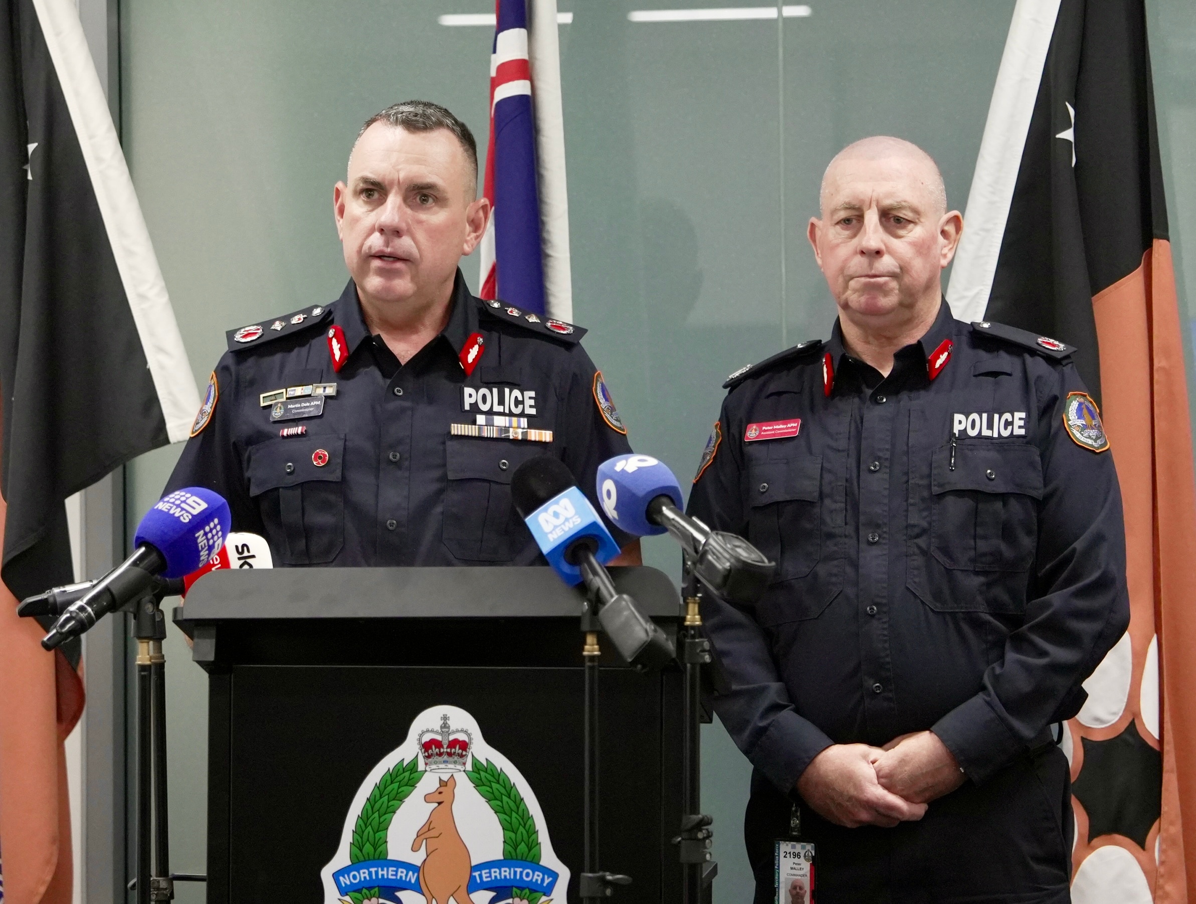 Two male police officers standing at a lectern and speaking into media microphones.