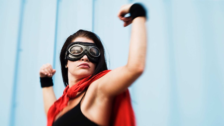 A woman wearing a cape flexes her bicep muscles in a show of strength