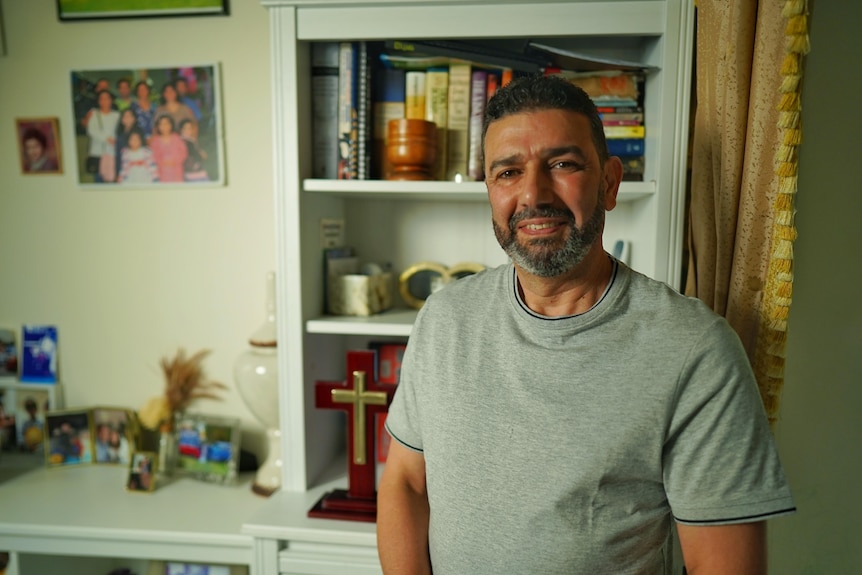 Man wearing a grey shirt standing in front of a bookshelf.