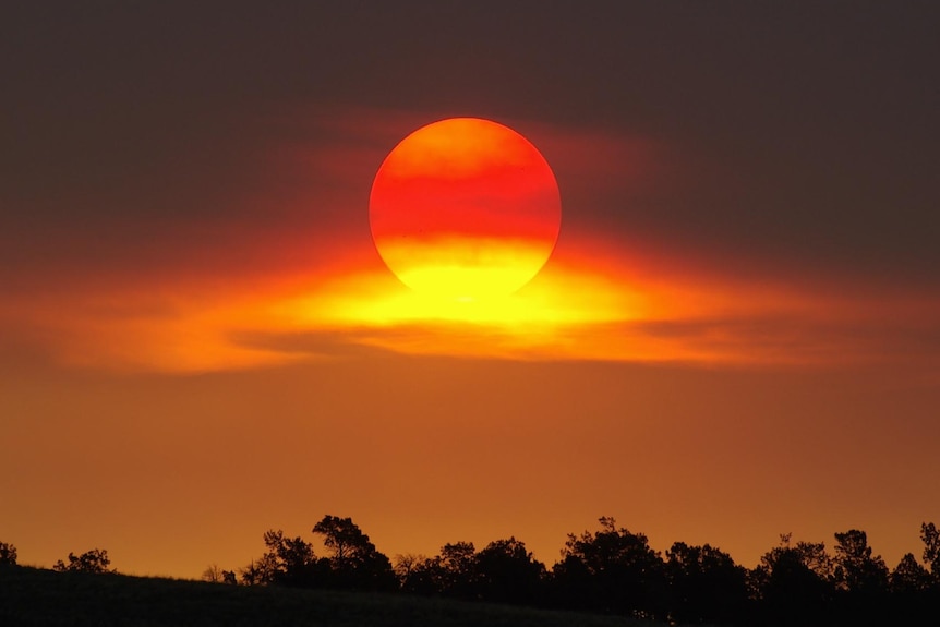 The setting sun appears through clouds.