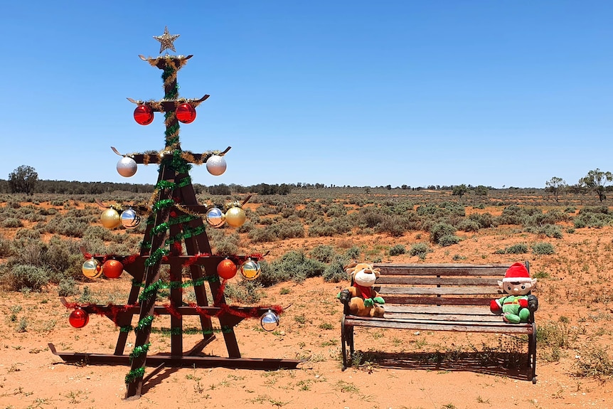 a rusted piece of farm equipment decorated like a christmas tree and a bench with toys sitting on it