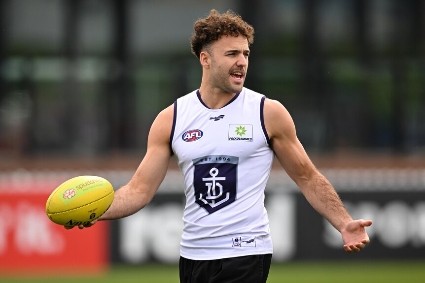 A Fremantle Dockers player at training holding an Australian rules football.