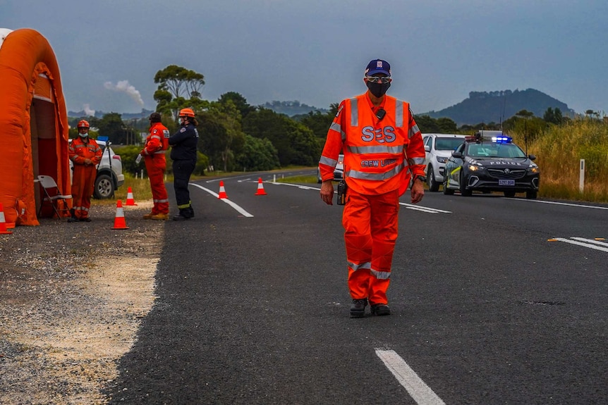 People wearing orange coloured uniforms walk on the side of a road next to police cars.