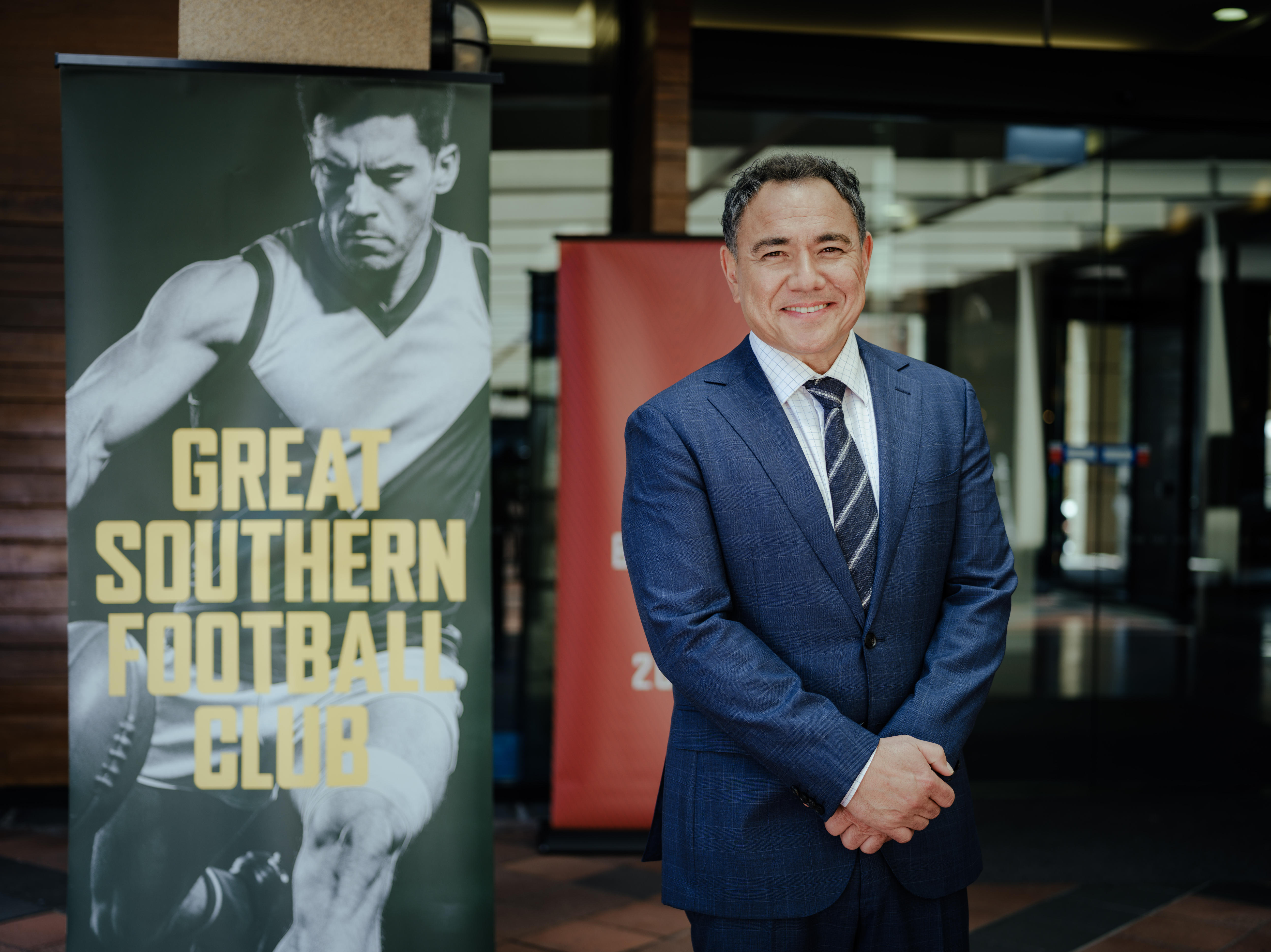 Sam smiles at the camera as he stands beside a banner featuring a footballer and the words Great Southern Football Club. 