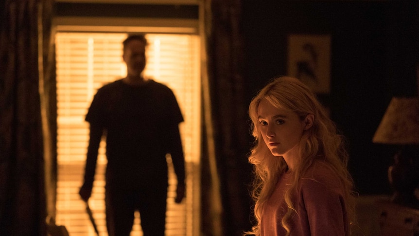 A scene from the movie Freaky with Kathryn Newton, a teen girl, in the foreground and a menacing killer in the background