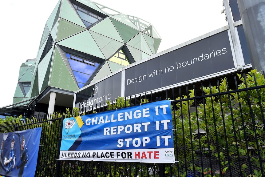 A banner with a message 'Challenge It Report It Stop It, Leeds No Place For Hate' hangs outside a cricket ground.