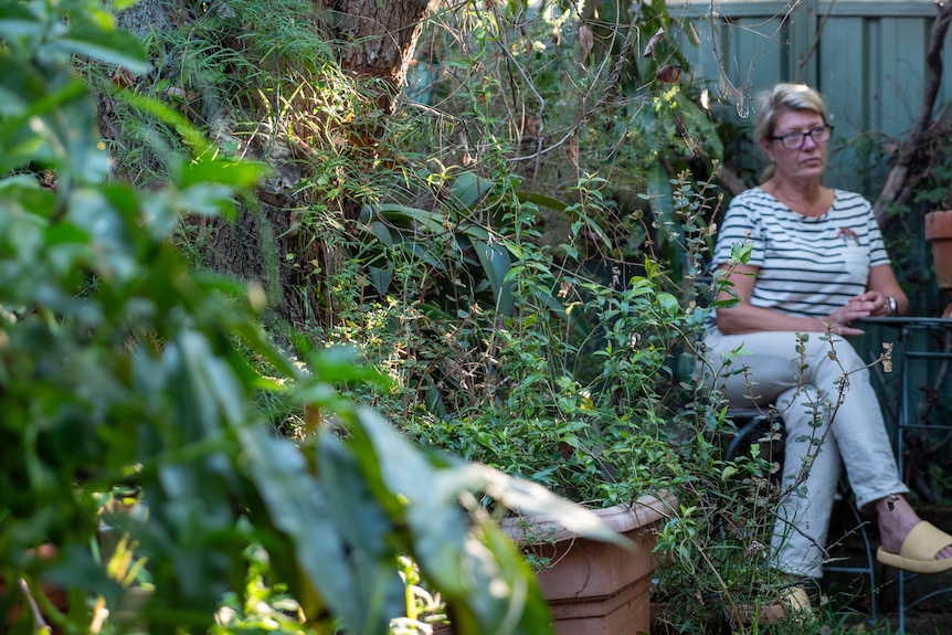Donna seduta in un cortile pieno di cespugli e alberi