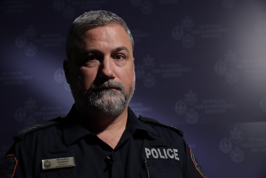 a male police officer with grey facial hair in uniform in a dark room
