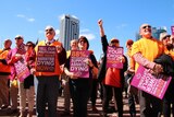 A crowd of people holding posters rallies outside State Parliament in Perth under a blue sky.