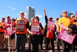 A crowd of people holding posters rallies outside State Parliament in Perth under a blue sky.