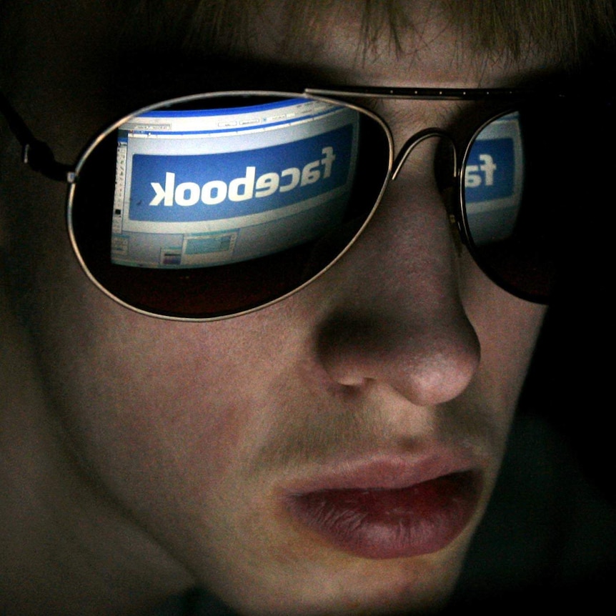 A youth looks at a computer with Facebook logo on it.