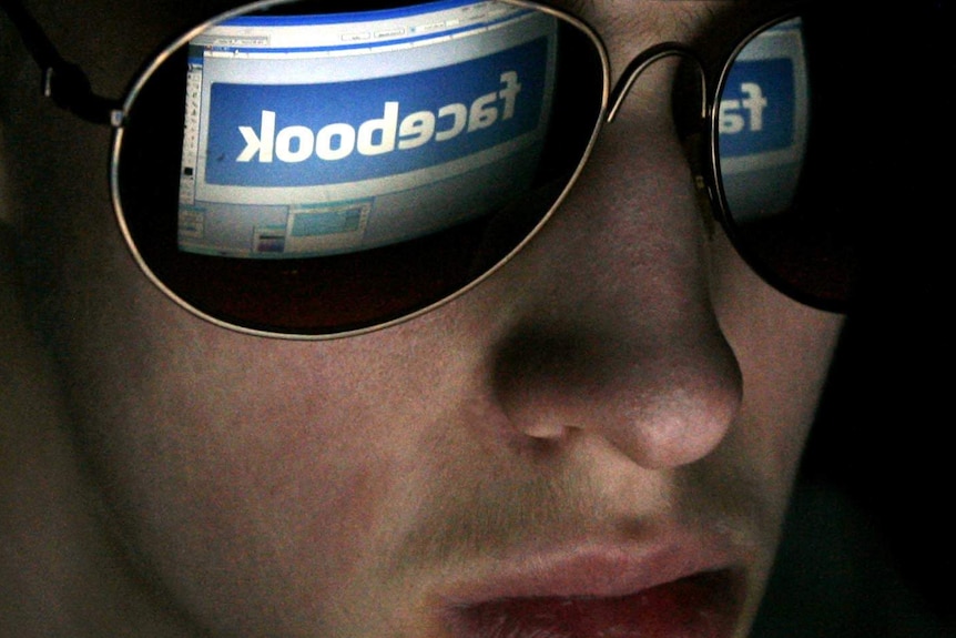 A youth looks at a computer with Facebook logo on it.