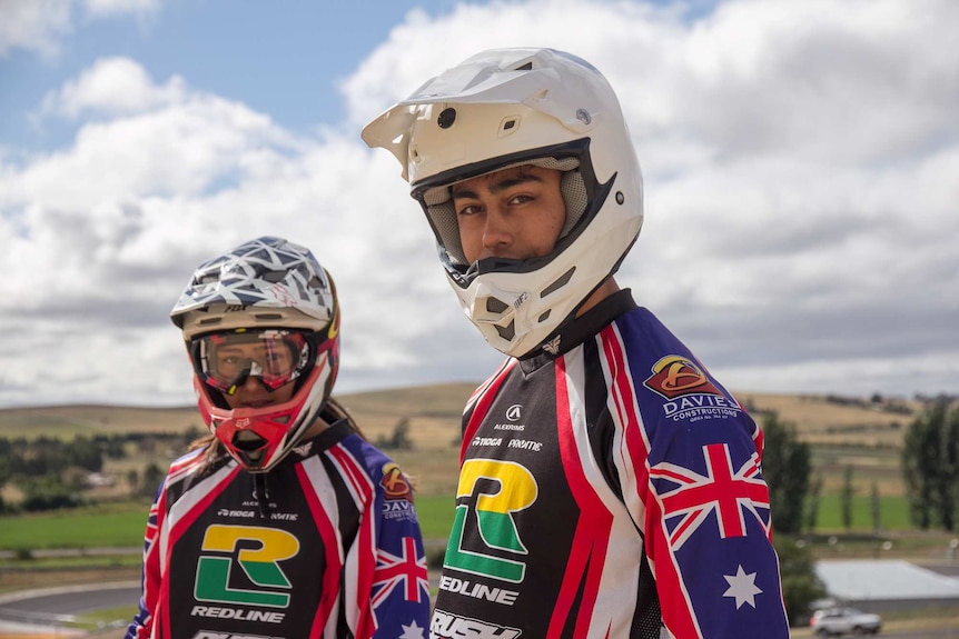 A teenaged girl and boy in BMX helmets and gear