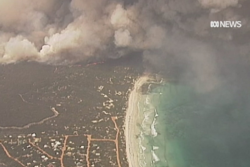 Smoke coming from land near a town on the sea with a beach