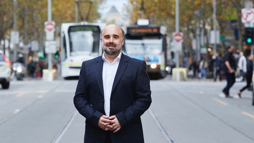 A man stands in the middle of a Melbourne street with trams in the background